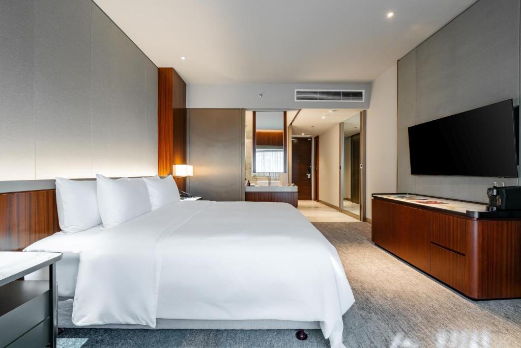 A large-bed room with a wall-mounted television and the entry corridor visible beyond.