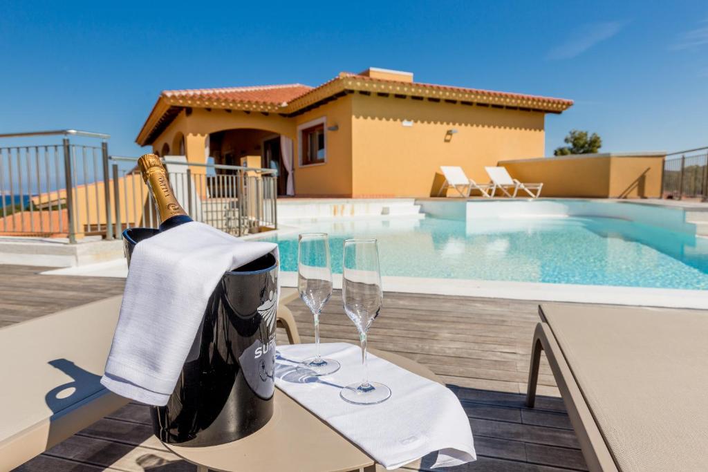 a bottle of wine and two glasses on a table by a swimming pool at Hotel Marana in Golfo Aranci