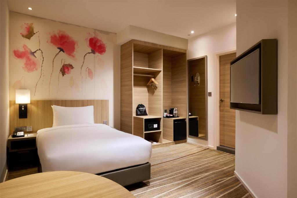 A compact guest room with a single bed, wall-mounted television, and open storage.