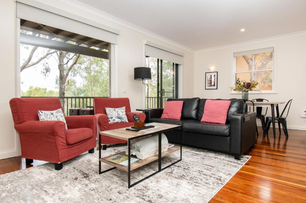 a living room with a black couch and red chairs at Villa in the Valley in Pokolbin