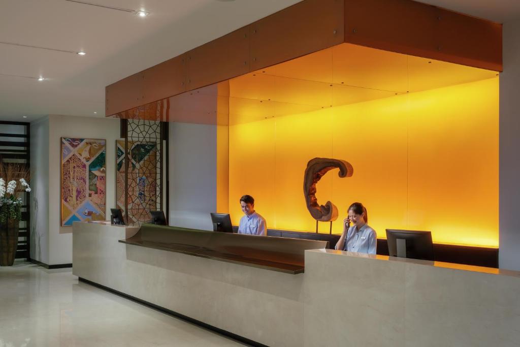 A reception desk with two staff members beneath a vivid amber-lit wall.
