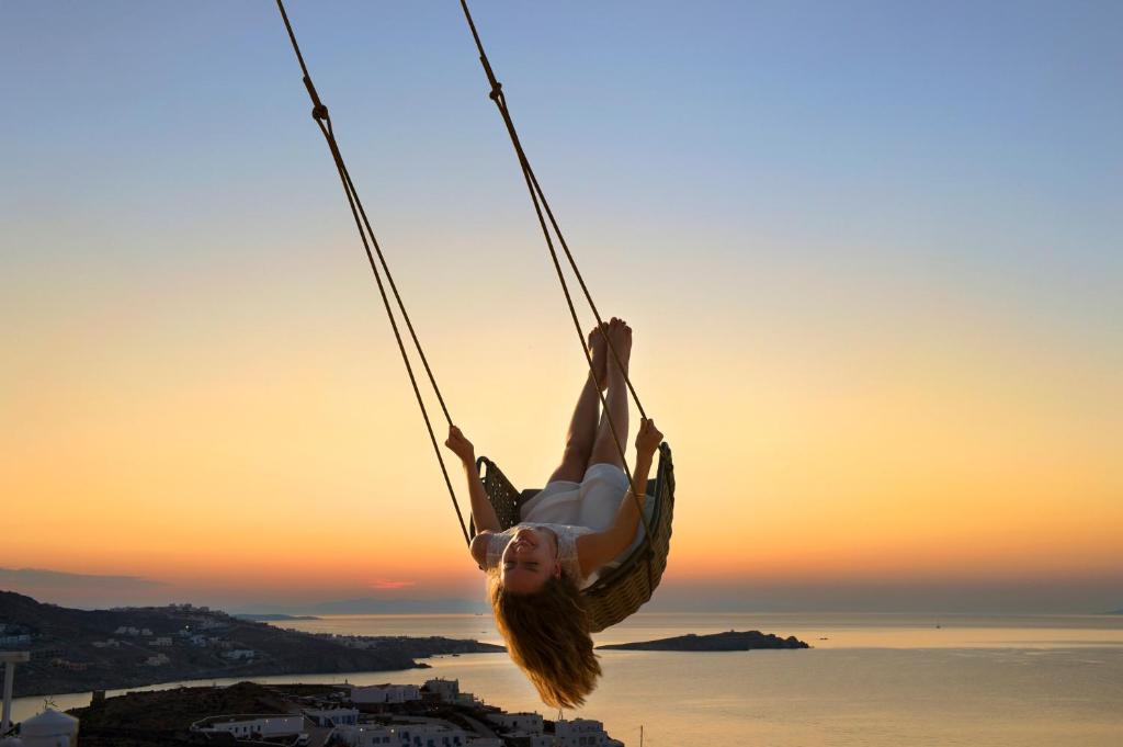 a girl is hanging on a rope swing at sunset at Myconian Naia - Preferred Hotels & Resorts in Mikonos