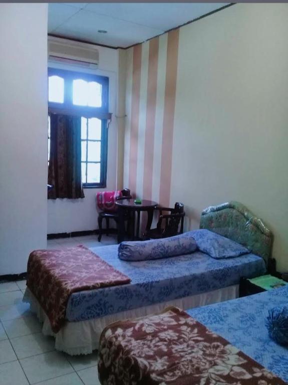 a room with two beds and a table and a window at Hotel Permata Inn Ball Room Seroja in Kualakapuas