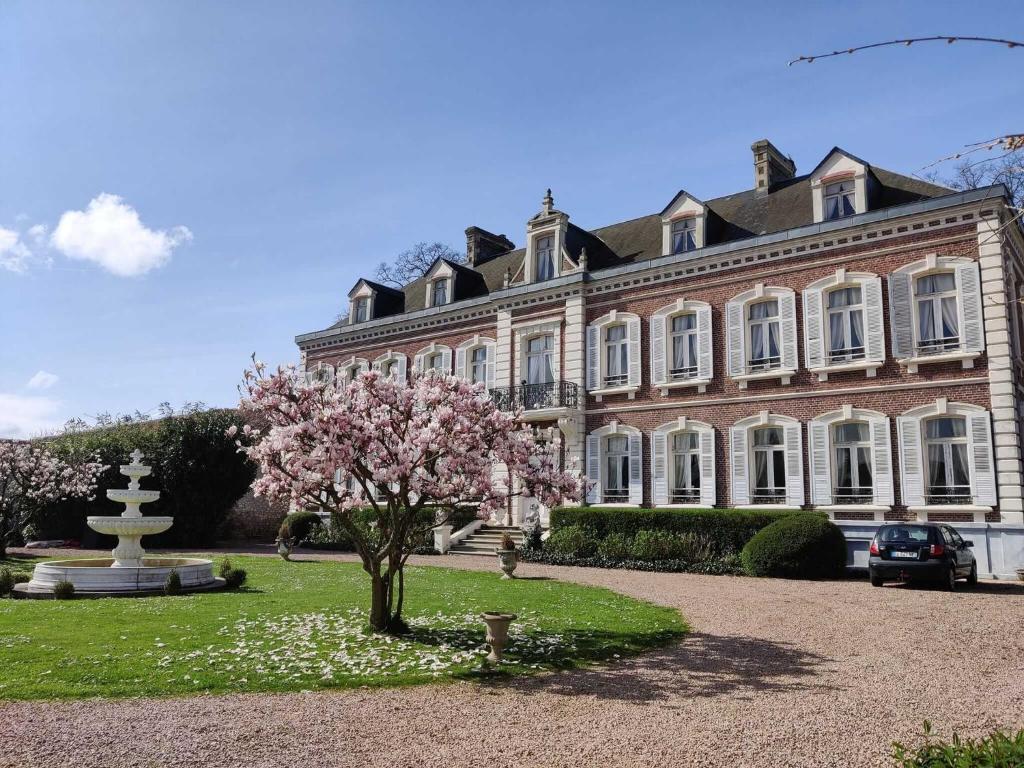 a large building with a flowering tree in front of it at Château de Beaucamp - Castel des anges in Wailly-Beaucamp