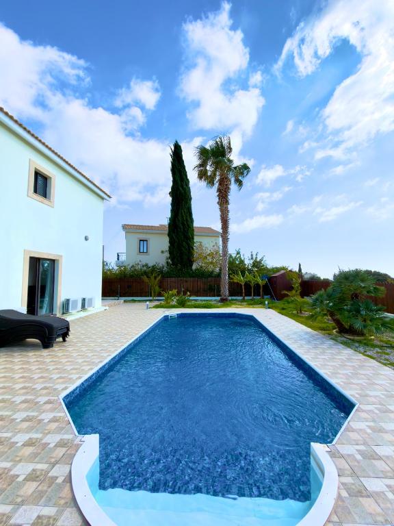 a swimming pool in a backyard with a house and palm trees at Casa Elea in Kouklia