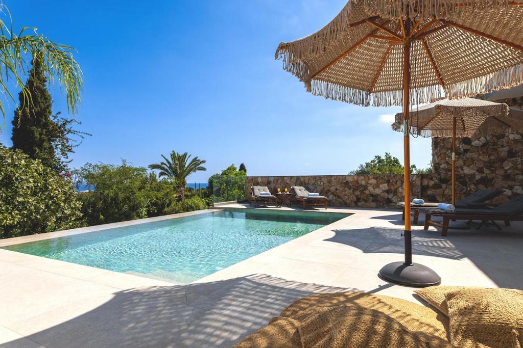 a swimming pool with an umbrella and some chairs at Orama Estate in Koskinou
