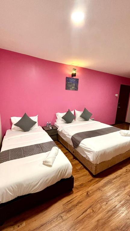 two beds in a room with a pink wall at City Hub Hotel Sitiawan in Sitiawan