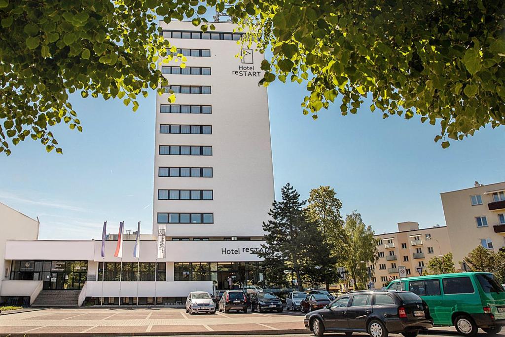 ein großes weißes Gebäude mit auf einem Parkplatz abgestellten Autos in der Unterkunft Hotel reSTART Superior in Jičín