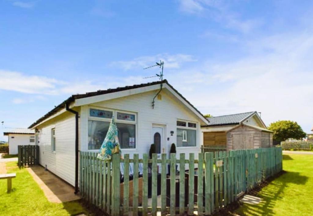 a small white house with a green fence at Sea Breeze Holiday Chalet in Bridlington