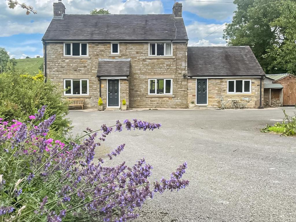 a stone house with purple flowers in front of it at Mill Lea Cottage in Leek
