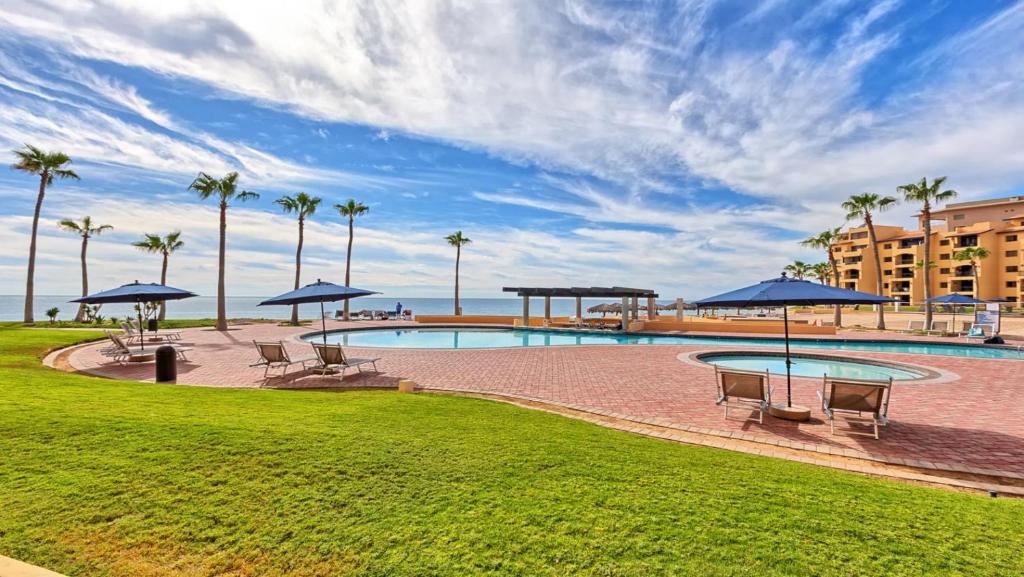 a swimming pool with benches and umbrellas and palm trees at Ground Floor 2BR Beachfront - Steps to Pool - Princesa E104 - BeachBumCondos in Puerto Peñasco