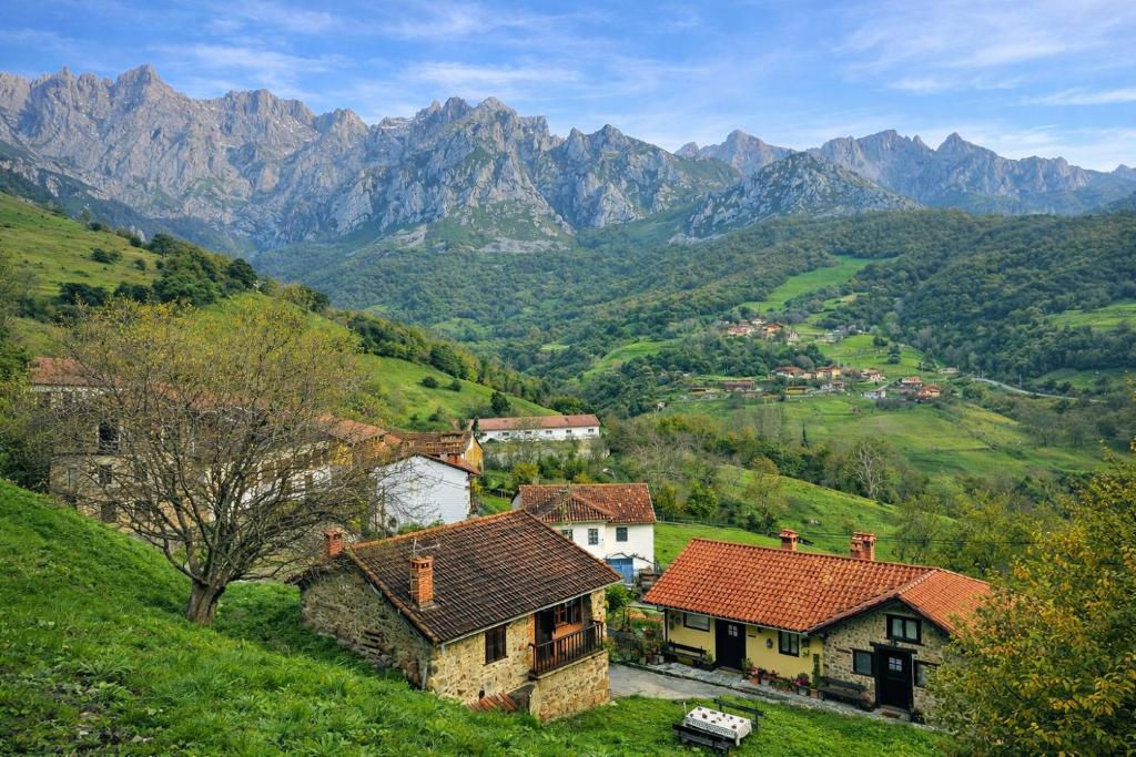 a village on a hill with mountains in the background at El Refugio de Redo - balcón a los Picos de Europa in Camaleño