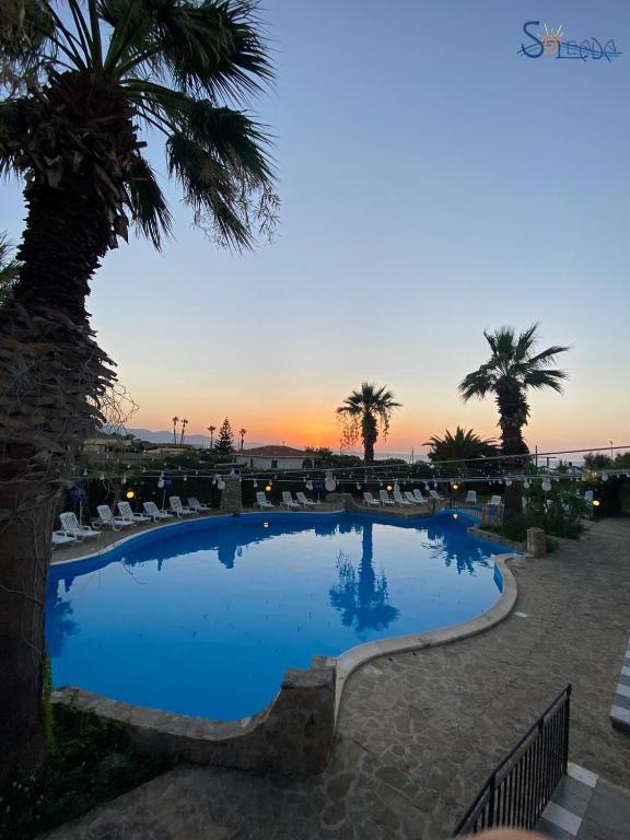 a swimming pool with palm trees and a sunset at Soleada Club in Campofelice di Roccella