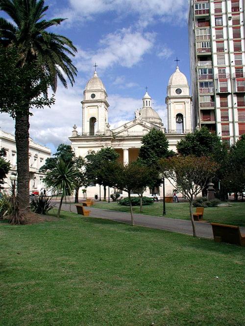 a large white building with a palm tree in a park at Plaza Mitre, departamento 2 dormitorios in San Nicolás de los Arroyos