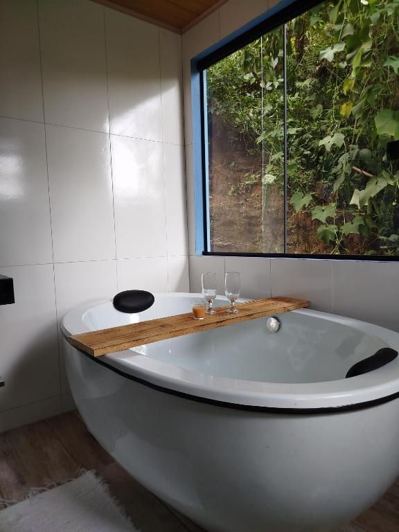 a bath tub with two wine glasses and a window at Chalé Studio Haven, microcasa com Mezanino e banheira in Lumiar