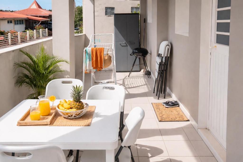 a white table and chairs on a balcony with a bowl of fruit at T3 climatisé avec terrasse proche plages in Rivière-Pilote