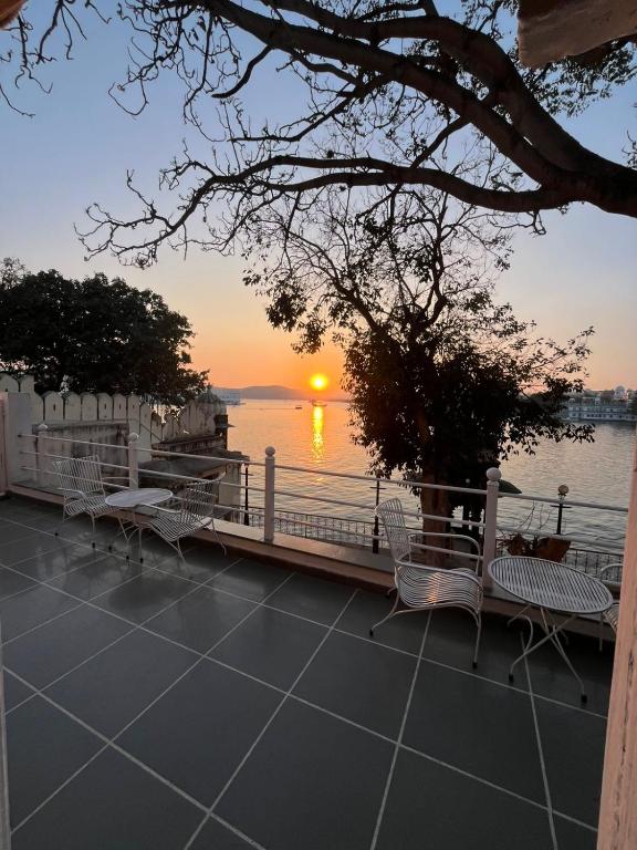 a sunset over the water with tables and chairs at Paddy's Loft The Lake B&B in Udaipur