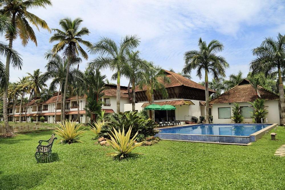 a resort yard with a swimming pool and palm trees at Manor Backwater Resort in Kumarakom