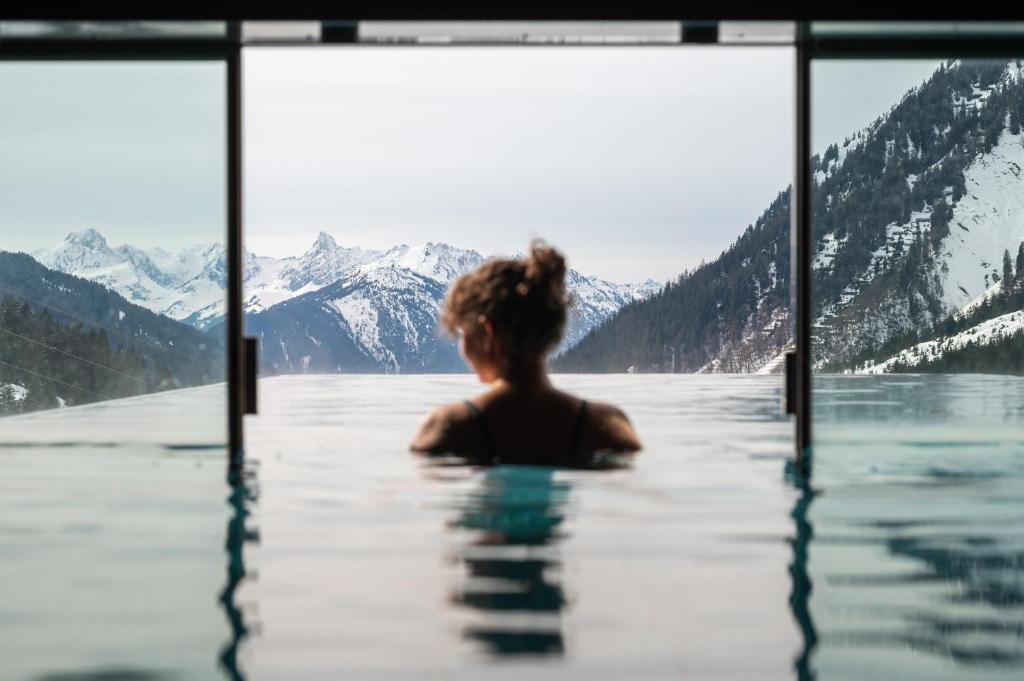 a woman sitting in a swimming pool with mountains at Wohlfühlhotel Hubertushof am Arlberg - Ski-In & Ski-Out - Sky Pool in Stuben am Arlberg