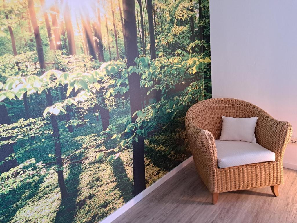 a wicker chair in a room with a forest mural at Ferienwohnung Wandelweg in Kamp-Lintfort