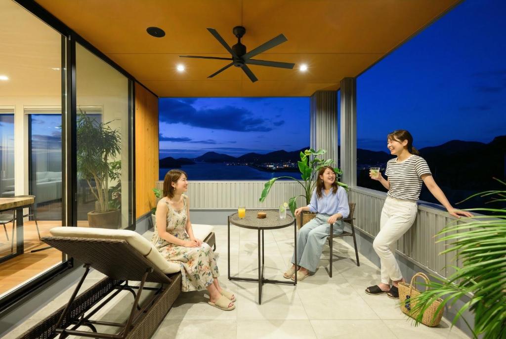 three women sitting on the balcony of a house at 父母ヶ浜リゾートヴィラ Senja in Mitoyo