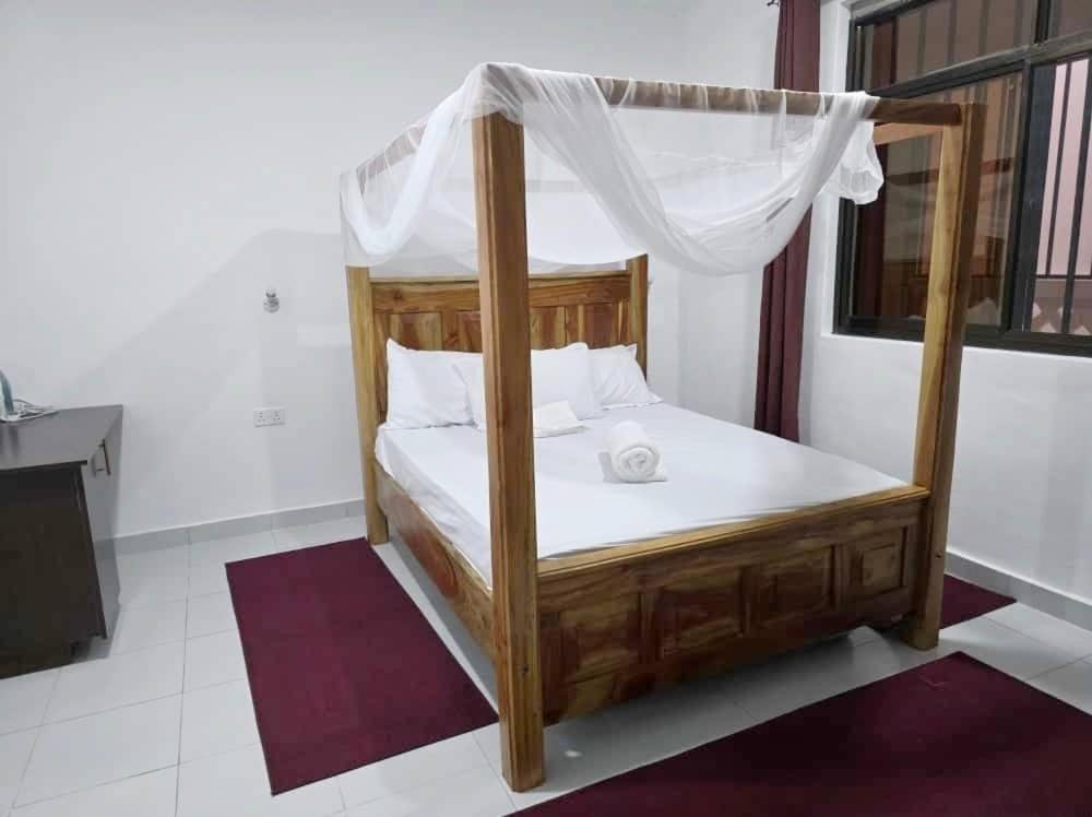 a wooden bed with a canopy in a room at TajiS Diani Chic 1 BR with swimming pool in Diani Beach