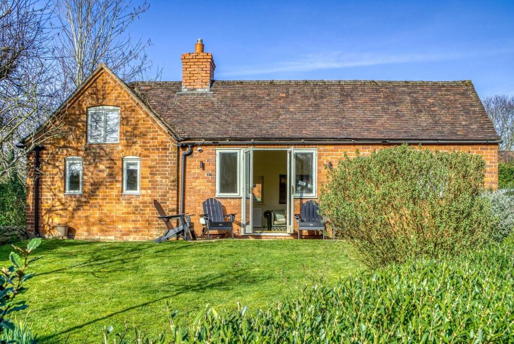 a brick house with two chairs on a lawn at Gleanings Cottage in Bredon