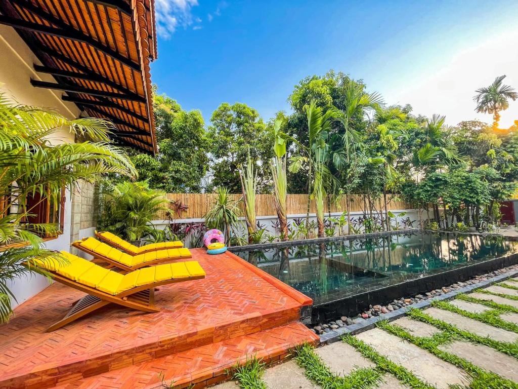 a patio with yellow chairs and a swimming pool at Isann Suites in Phumĭ Réach Born (1)