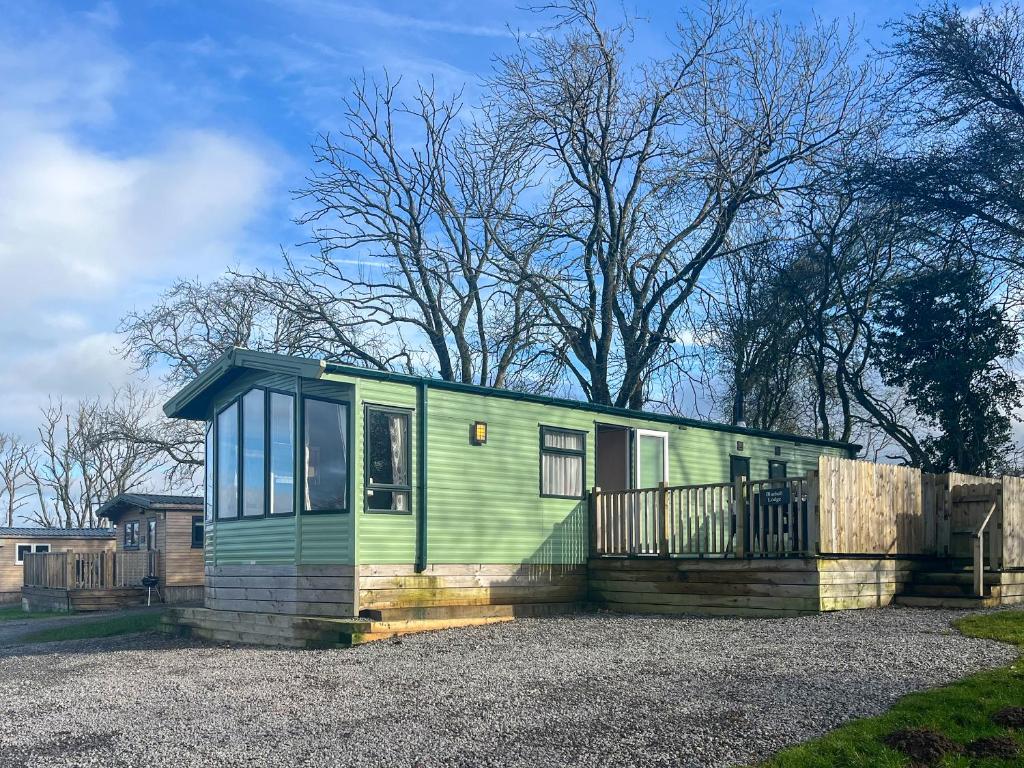 a green tiny house on a gravel lot at Bluebell Lodge - Uk51382 in Wigton