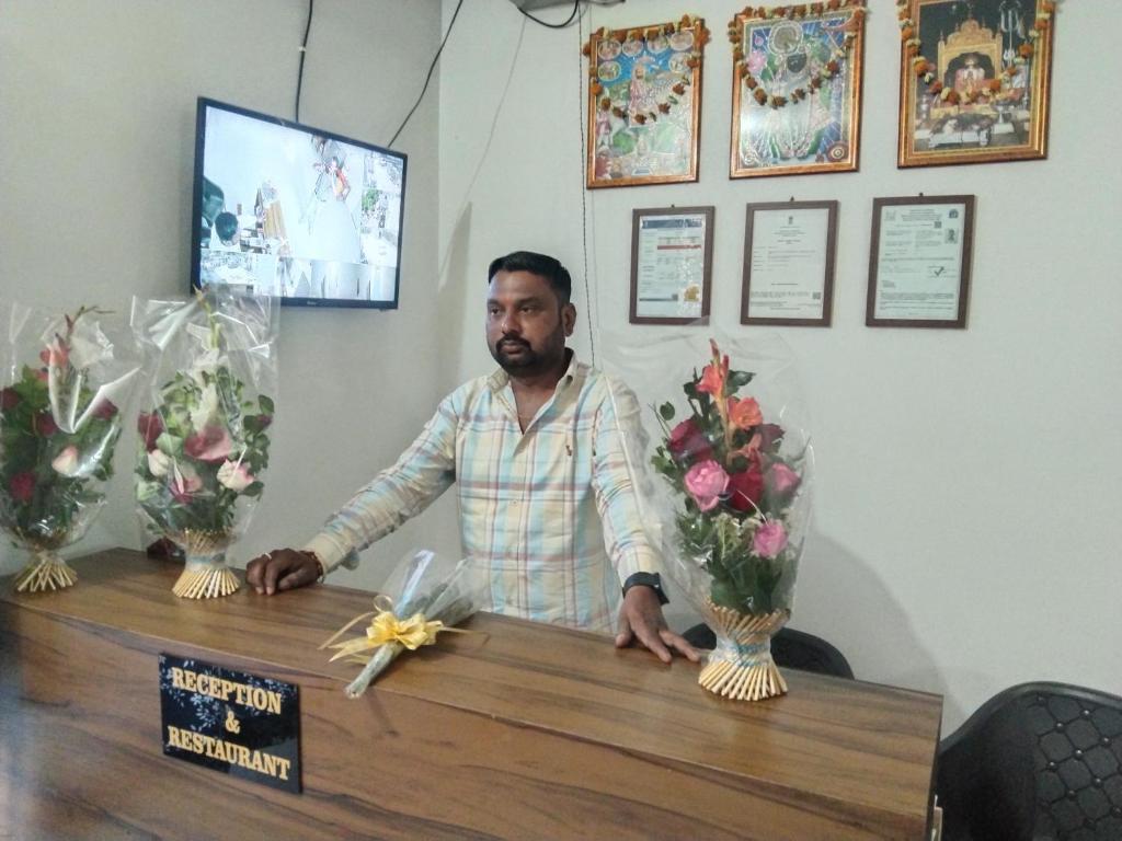 a man standing behind a counter with flowers in vases at Akshay Hotel in Bikaner