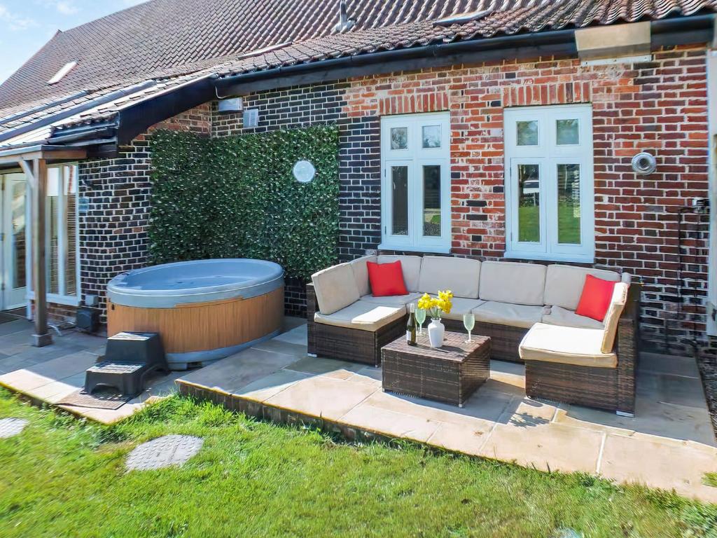 a patio with a hot tub next to a brick house at Holly Barn in Ashwellthorpe