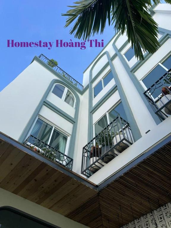a white building with balconies and a palm tree at Homestay Hoàng Thi in Phan Thiet