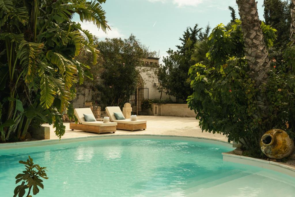 a swimming pool with two lounge chairs and a palm tree at Masseria Messapia Wine Resort & Spa Salento in Mesagne