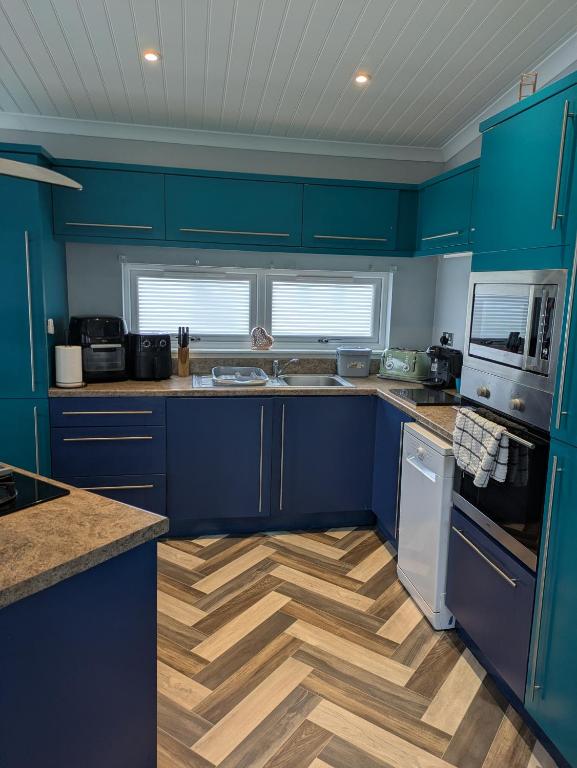 a kitchen with blue cabinets and a wooden floor at Unique 2 bed lodge lyons Robinhood in Rhyl