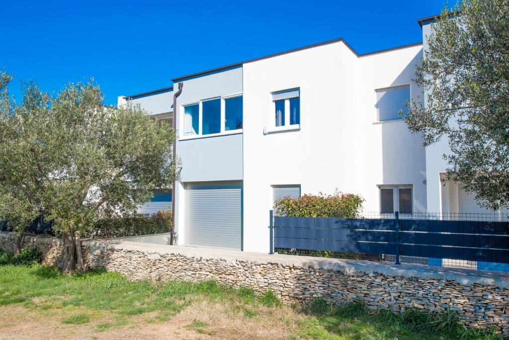 a white house with a stone wall and trees at Apartman Denis in Pula