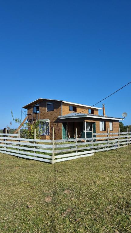 a house behind a white fence in a field at Casa grande el dao in Calbuco