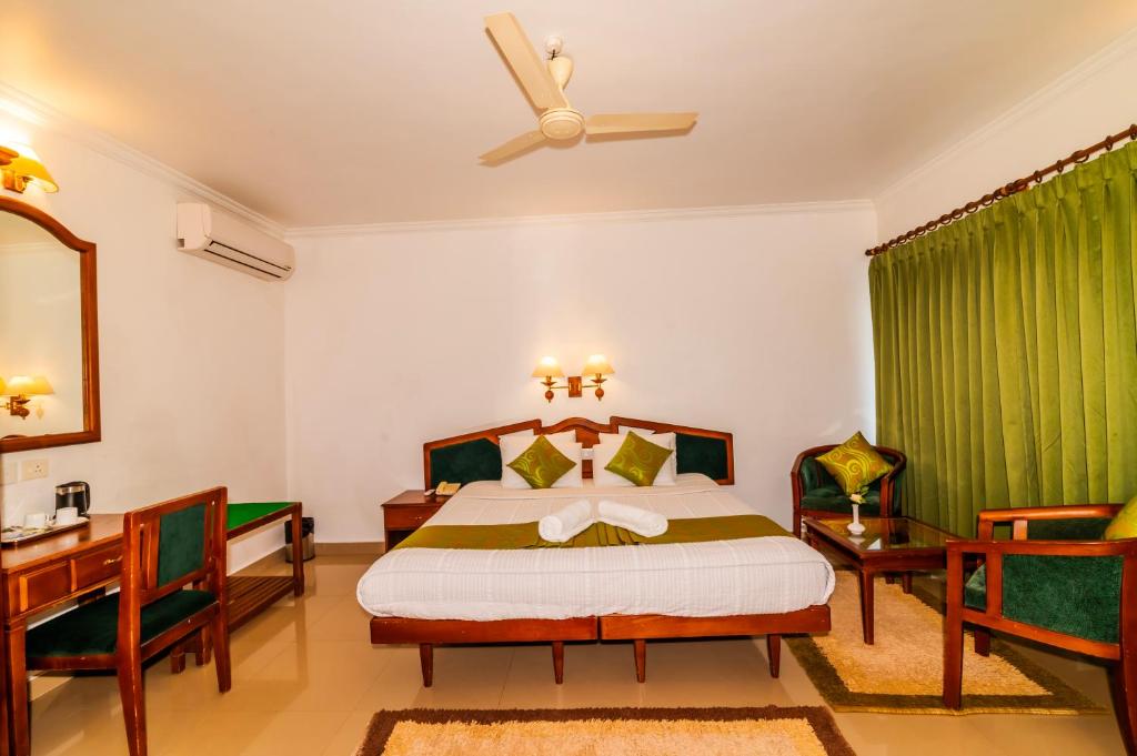 a bedroom with a bed and two chairs and a ceiling fan at Periyar Meadows Leisure Hotel in Thekkady
