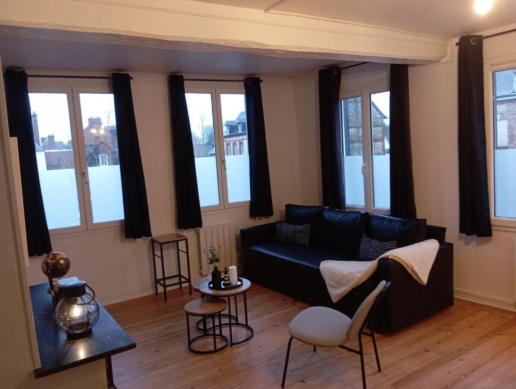 a living room with a black couch and some windows at Magnifique et Grand T3 au cœur de la Normandie in Saint-Victor-lʼAbbaye