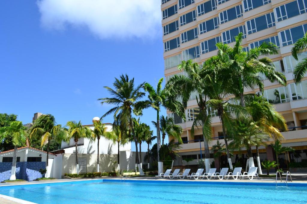 a swimming pool in front of a hotel with palm trees at Hotel Faranda Express Puerta del Sol Porlamar in Porlamar