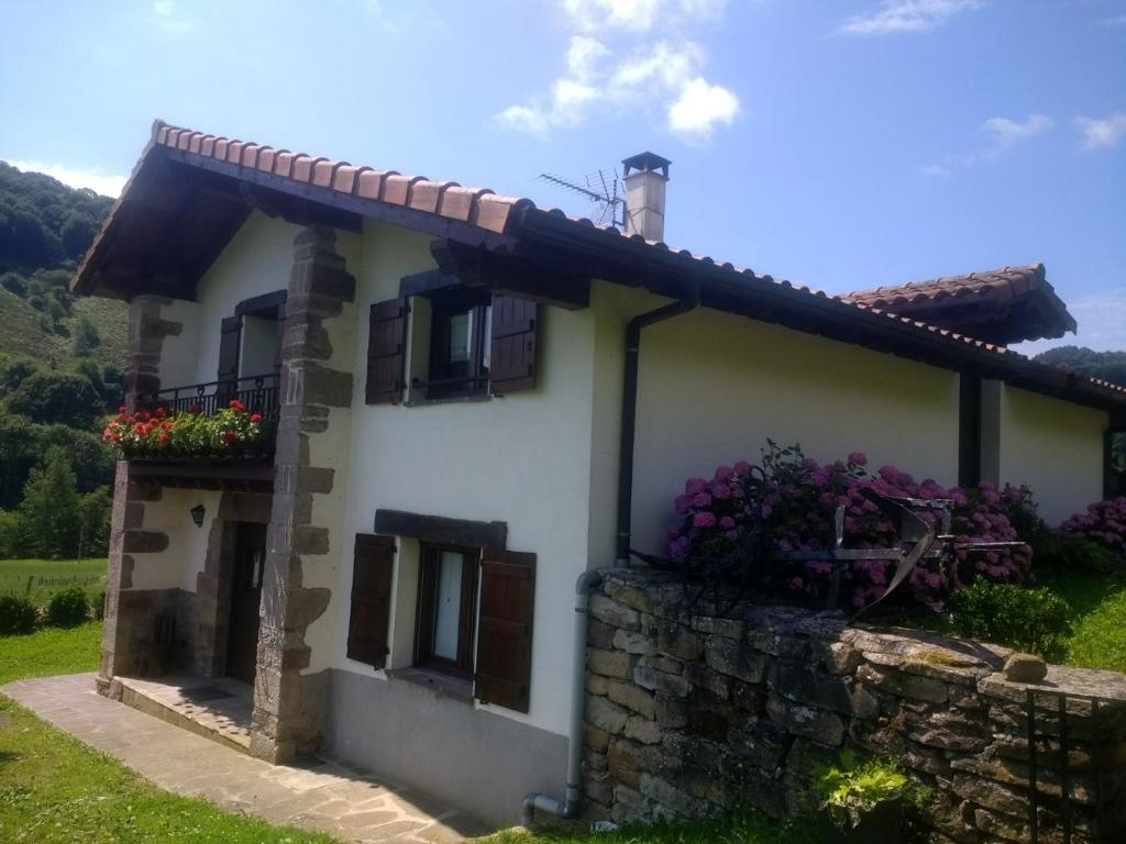 a white house with flowers on a stone wall at Alberroakoborda in Ituren