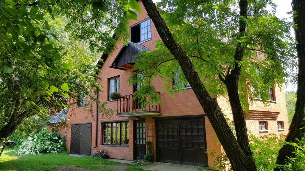a red brick house with a garage and trees at Namiņš Brīviņi in Jaunjelgava