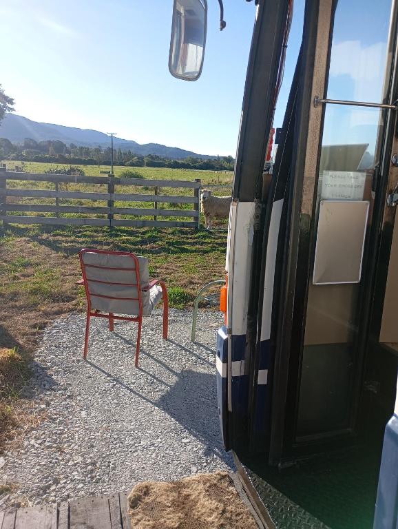 a chair sitting outside of a bus next to a fence at Cruzo The House Bus in Takaka