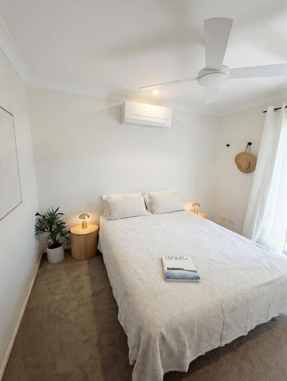a white bedroom with a bed with a book on it at Barefoot at Sunrise Guest Suite in Byron Bay