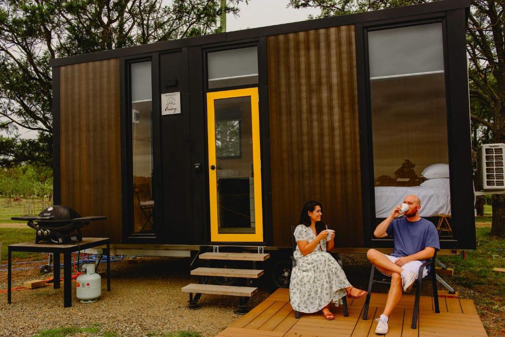 a man and woman sitting in front of a tiny house at Sunset Tiny House at Bluebush Estate X by Tiny Away in Rothbury