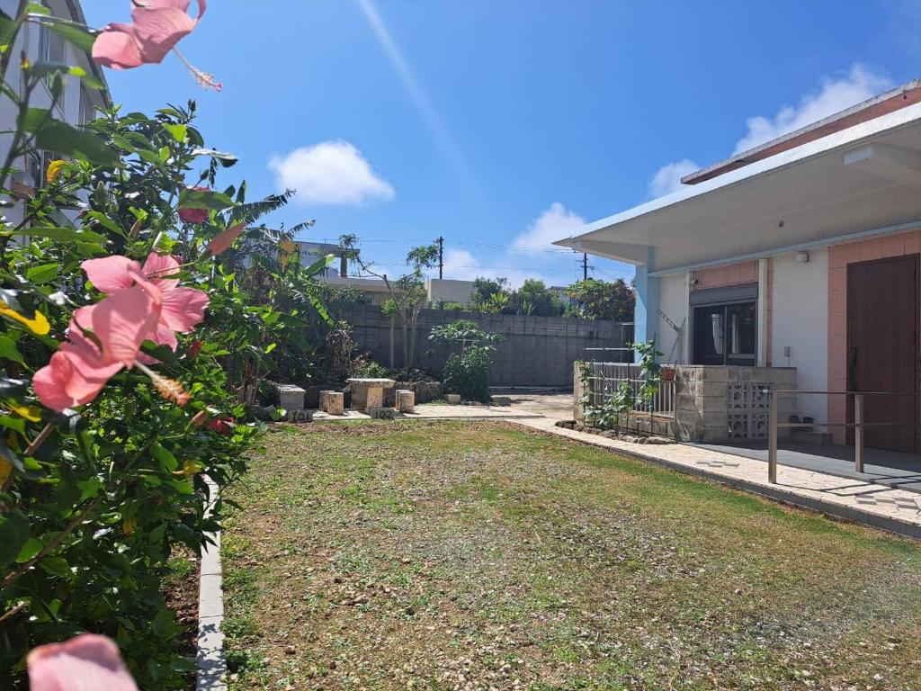 a yard in front of a house with pink flowers at ヴィラ結Miyakojima2 in Miyako-jima