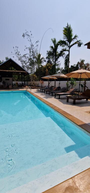 a large swimming pool with benches and umbrellas at Kingfisher House in Sangkhla Buri