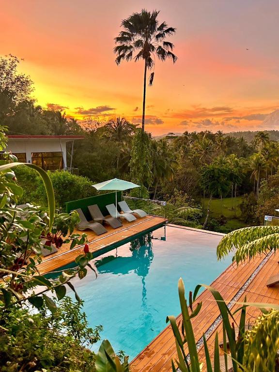 a pool with chairs and a palm tree and a sunset at Jinjer Resort in Cavinti
