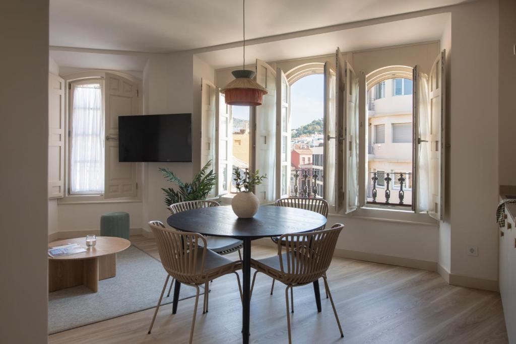 a dining room with a table and chairs and windows at Líbere Málaga Plaza del Siglo in Málaga