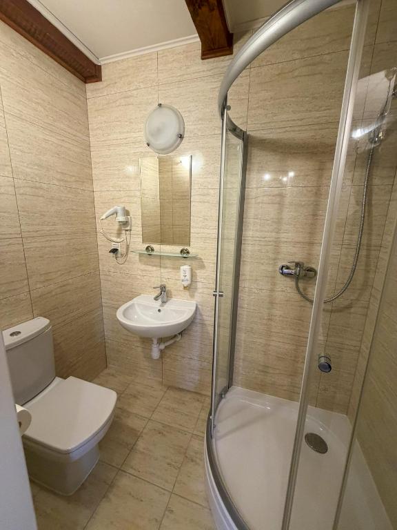 Small beige-tiled bathroom with corner glass shower, wall-mounted sink, toilet, and hairdryer.