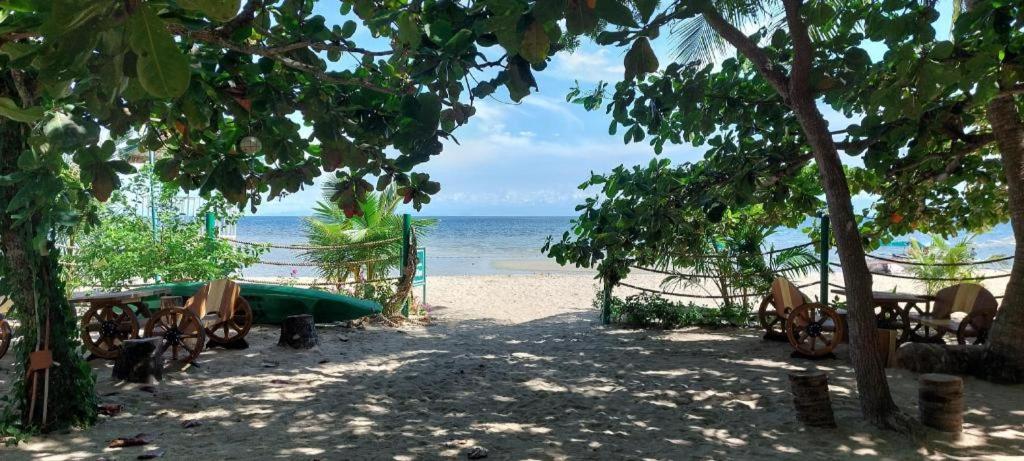 a beach with a hammock and a boat on the beach at Paseo Verde Beach Resort in Laiya
